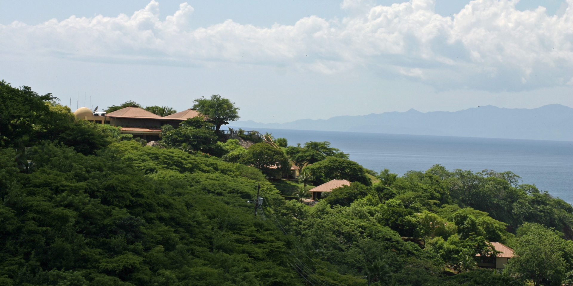 Distant view of Ocotal Beach Resort, displaying the club house, lush vegetation, duplex villas peeking through the foliage, and the breathtaking sea with mountains across the bay