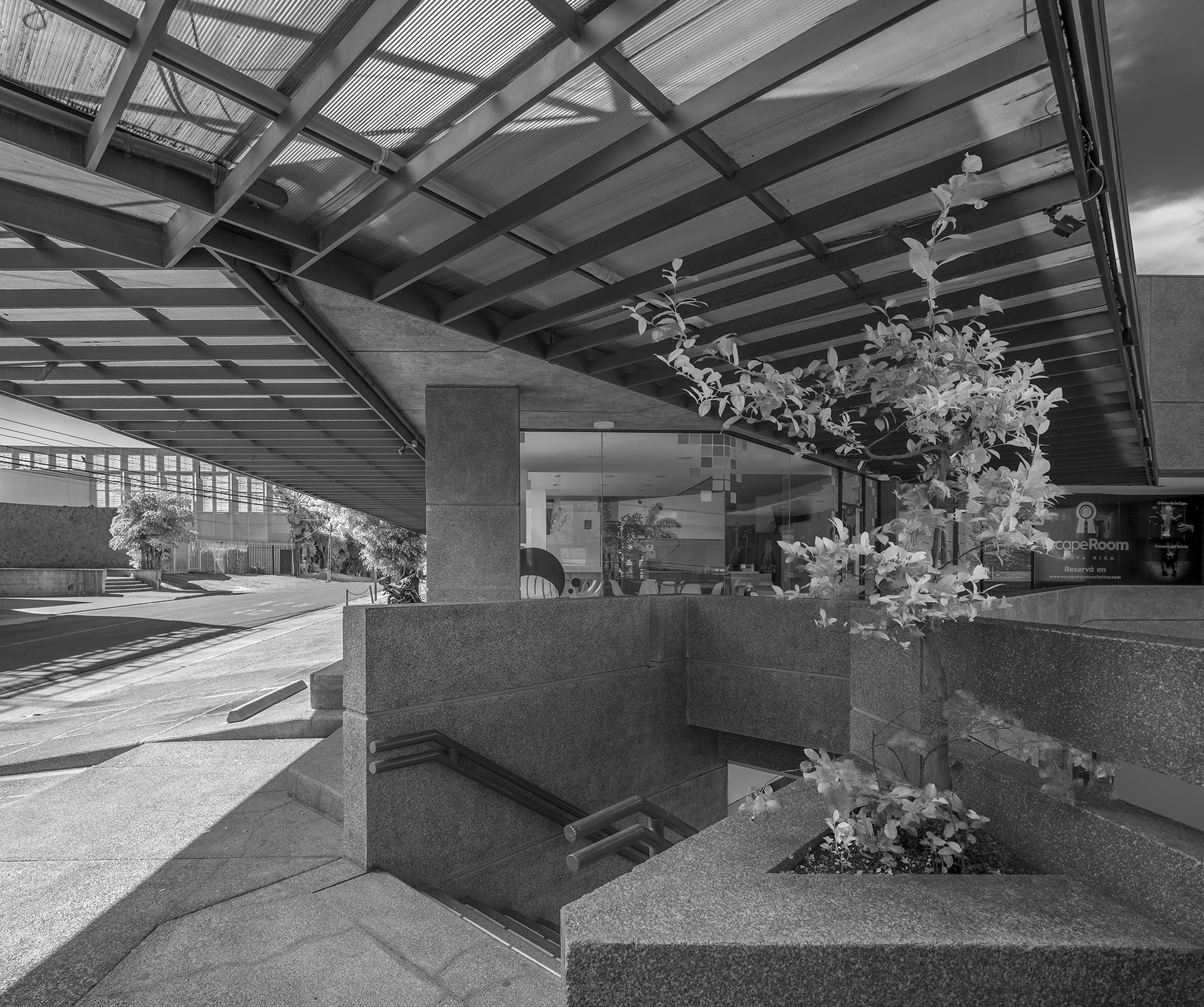 Close-up black and white photo of Plaza Rolex detailing the star-edge corner of a shop window and an exterior staircase under steel pergolas.