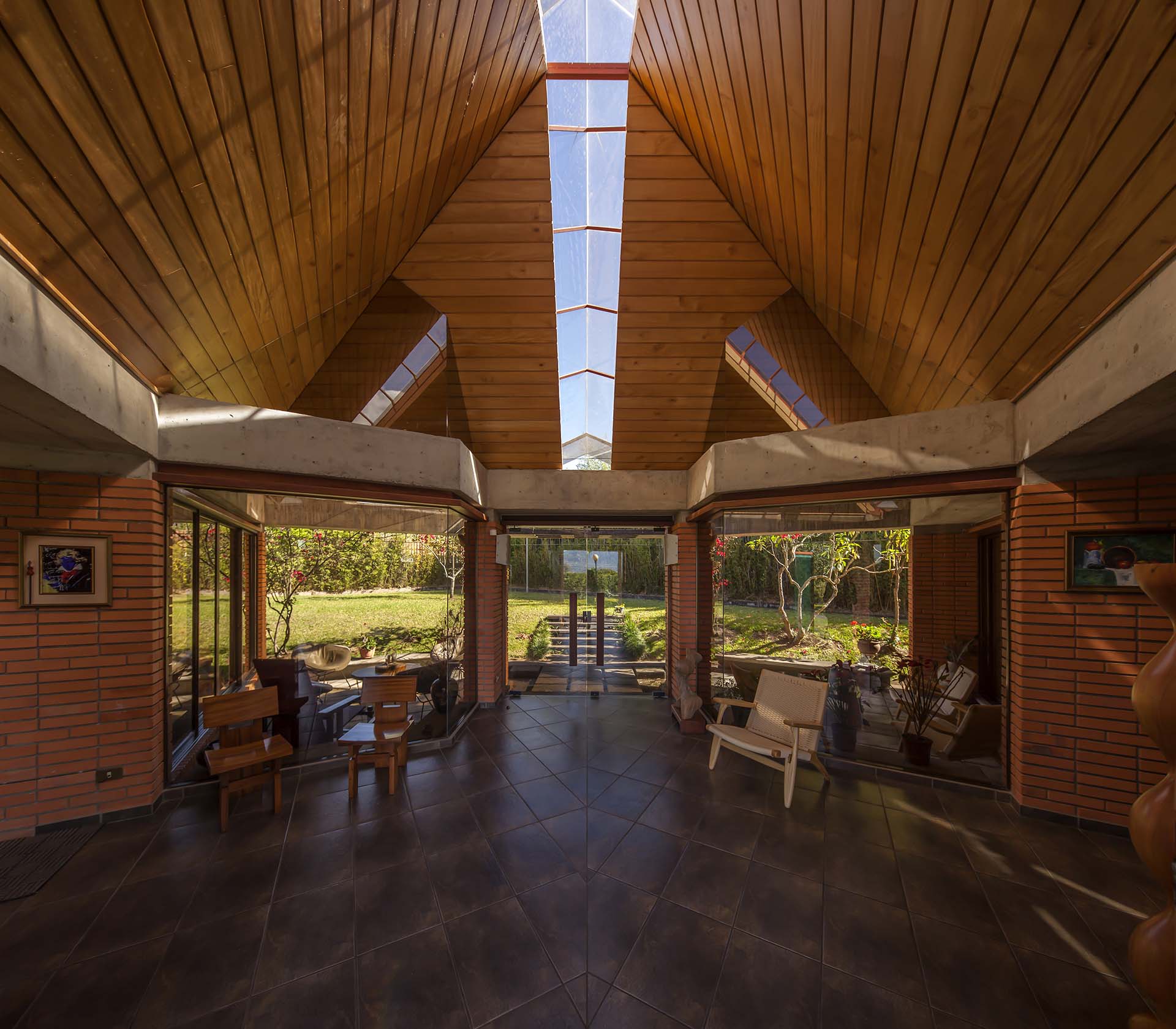 Symmetrical view from within the Soto House lobby, looking out towards dual terraces and the back garden. The dark grey floor, wooden ceilings with skylight, and wooden chairs built by the owner, exemplify Costa Rican architectural design
